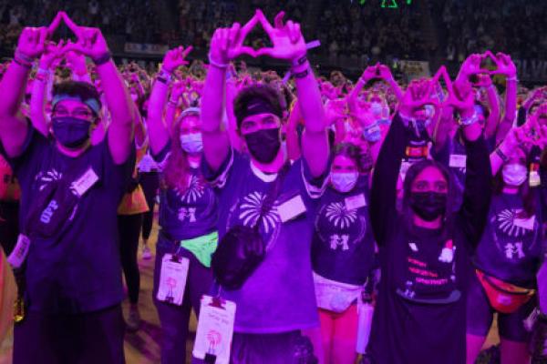 Several dancers at THON 2022 stand on the dance floor with their hands raised in the air, making diamond shapes with their fingers.