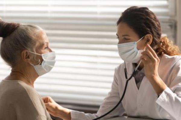 A doctor in a surgical mask hold a stethoscope as she listens to a patient’s heart.