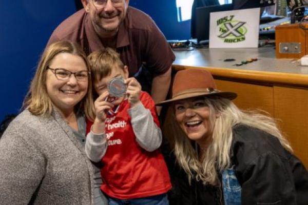 Three adults and one child pose for a photo in a radio studio, smiling.