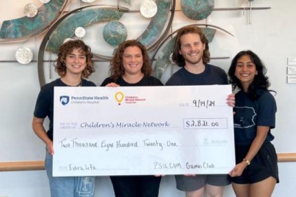 Four people smile for a photo while holding a large check from a fundraising event