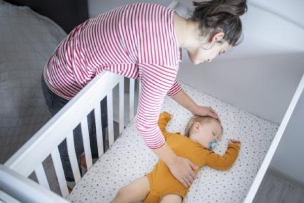 A mother puts her baby to sleep in a crib.