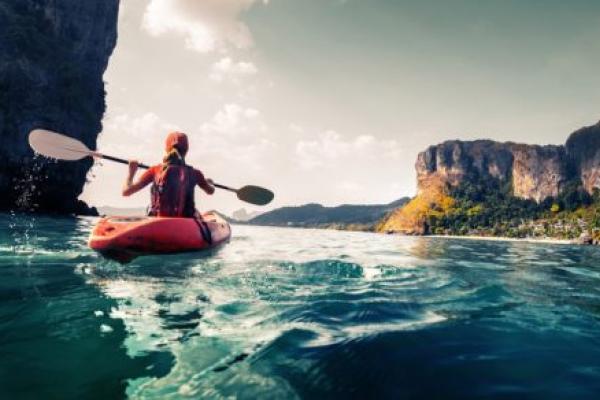 A woman paddles a kayak in a calm, tropical bay.