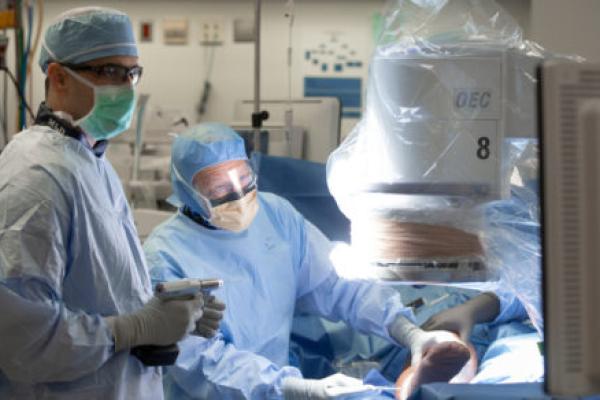 Two doctors in personal protective equipment stand next to an operating table with a patient on it.