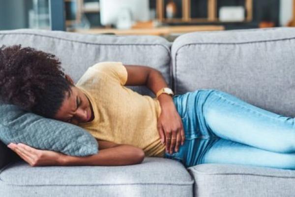 A young woman experiencing abdominal pain lies on the sofa at home.