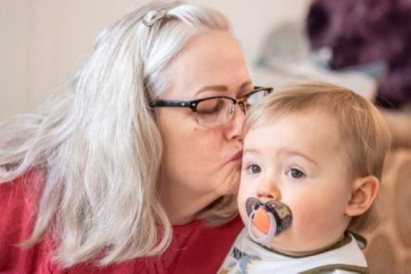 Woman leans over and kisses her infant grandson.